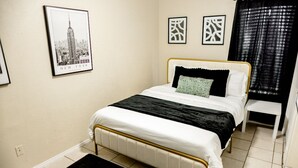 Un dormitorio ordenado con una cama, un pequeño banco y un cuadro enmarcado del Empire State Building en la pared.