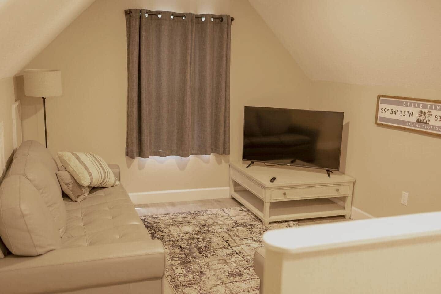 A living room with a television on a stand, a sofa, a patterned rug, and a window with curtains.
