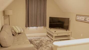 A living room with a television on a stand, a sofa, a patterned rug, and a window with curtains.