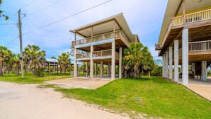 A two-story building with a balcony on the upper floor, surrounded by palm trees and a clear sky. - Cedar Island Coastal Retreat | Gulf Access, Huge Deck & Fami (Taylor County)
