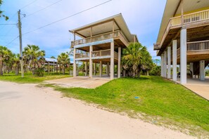 A two-story building with a balcony on the upper floor, surrounded by palm trees and a clear sky.