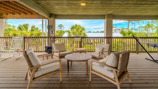A covered outdoor seating area with wooden furniture and a view of the ocean. - Cedar Island Coastal Retreat | Gulf Access, Huge Deck & Fami (Taylor County)