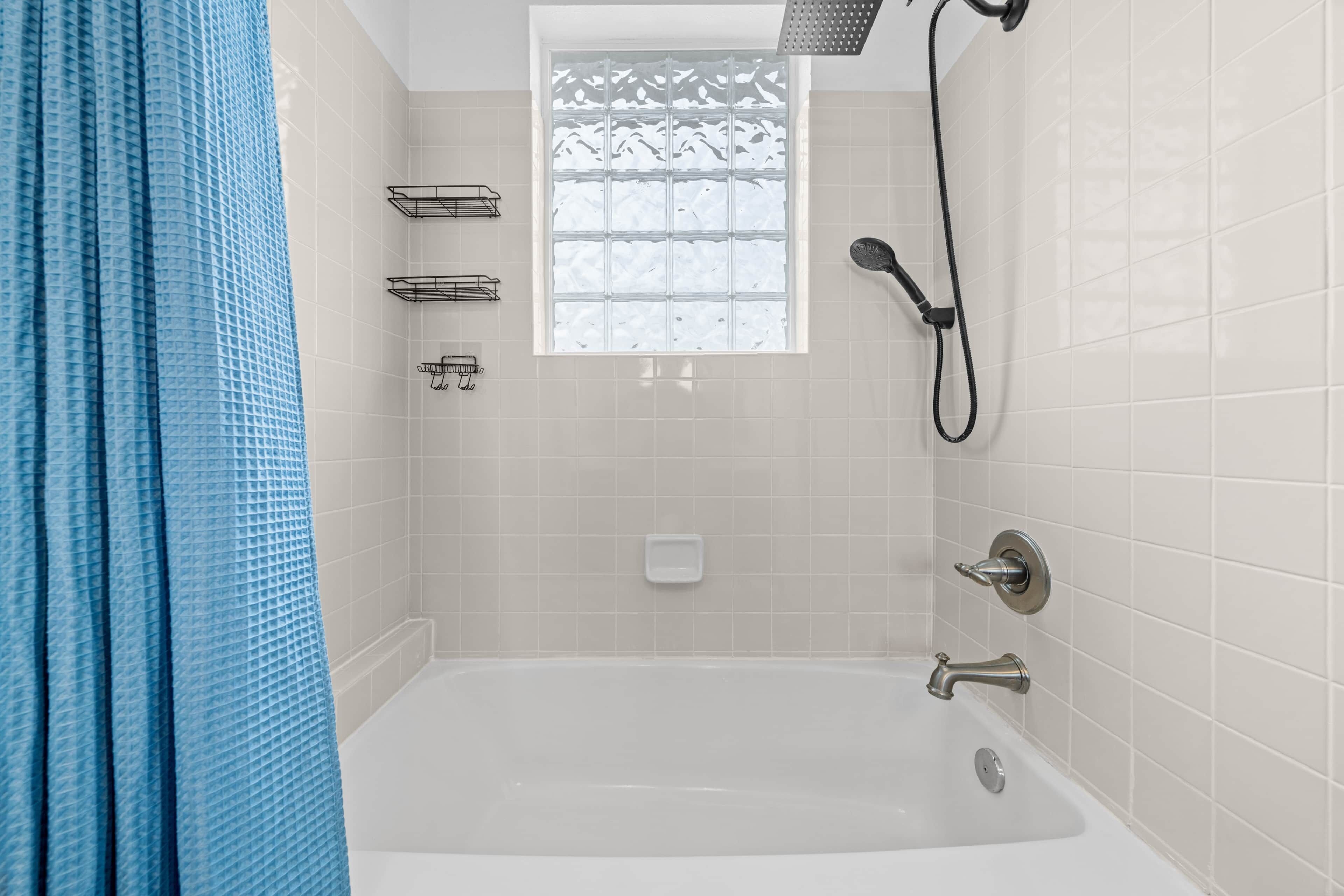 Een badkamer met een badkuip, douche en raam.