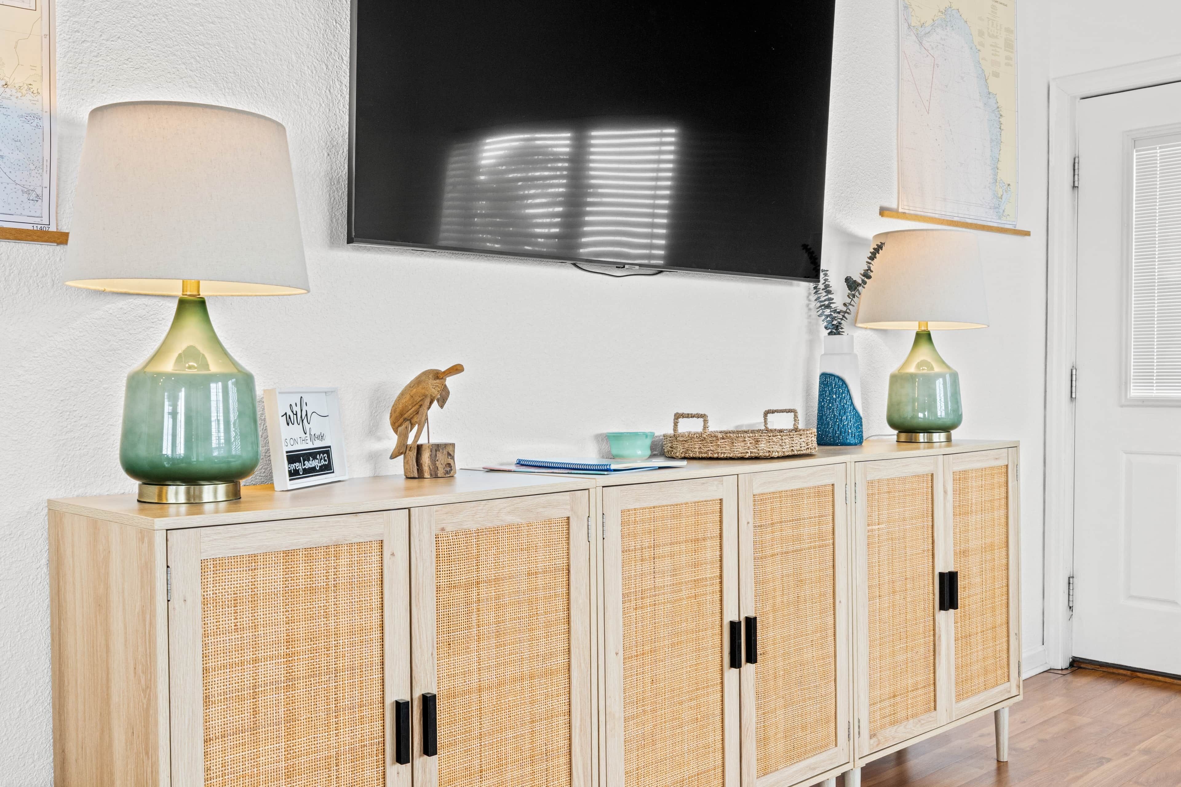 A wooden cabinet with woven doors, two lamps, a bird figurine, a framed sign, and a map on the wall.