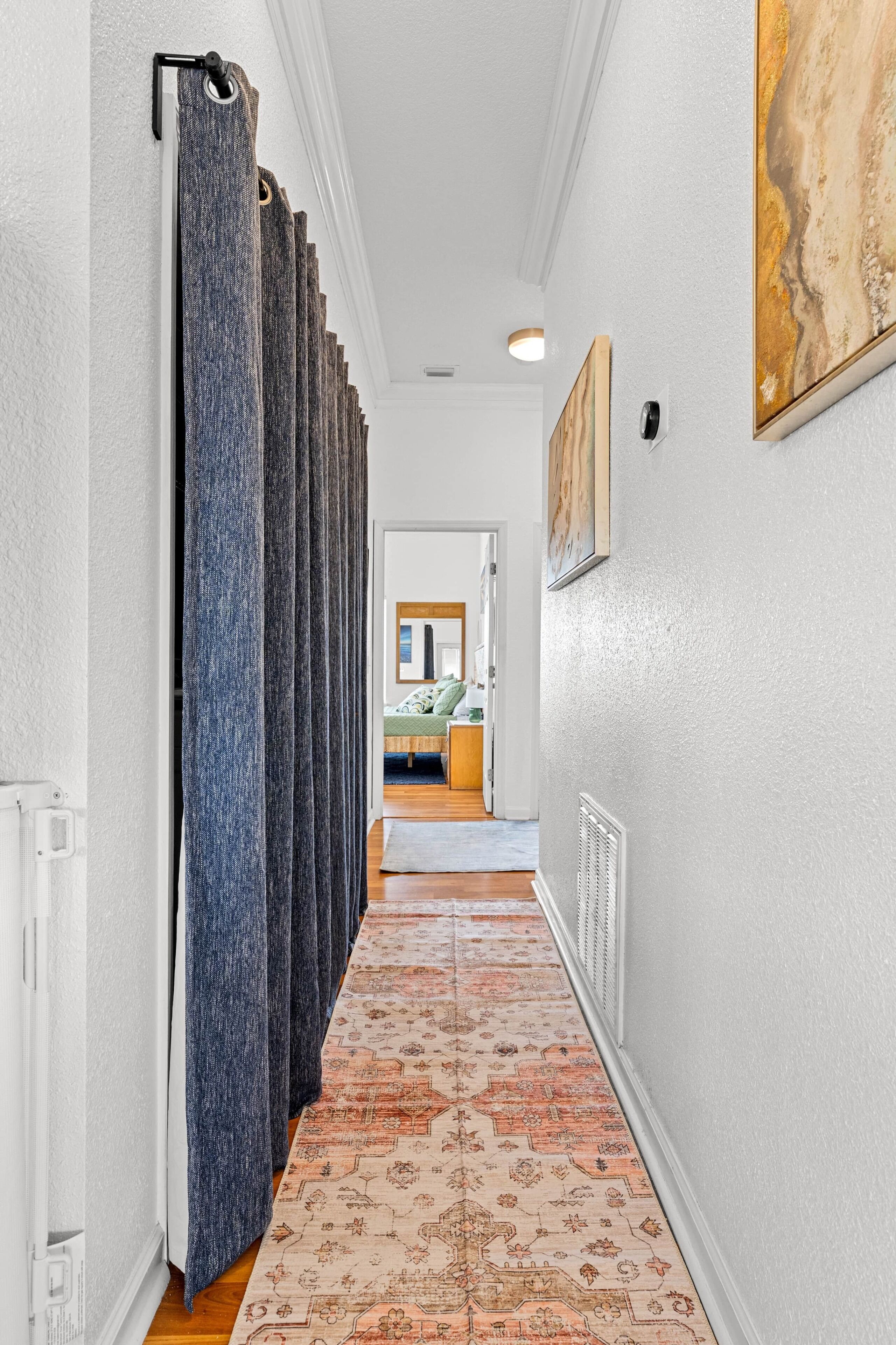 A hallway with a patterned carpet, a row of curtains, a radiator, and a painting on the wall.