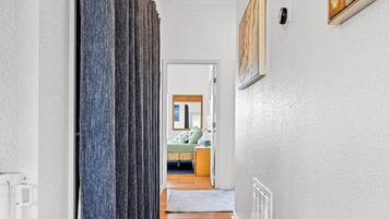A hallway with a patterned carpet, a row of curtains, a radiator, and a painting on the wall.