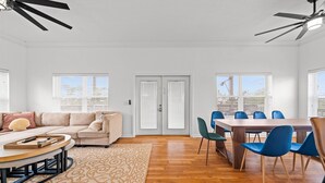 A modern living room with a sofa, a dining table with chairs, a ceiling fan, and a patterned rug. - Cedar Island Coastal Retreat | Gulf Access, Huge Deck & Fami (Taylor County)