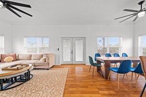 A modern living room with a sofa, a dining table with chairs, a ceiling fan, and a patterned rug.