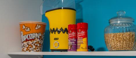A shelf with popcorn, a popcorn maker, and seasoning bottles.
