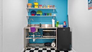 Een kleine keuken met een blauwe wand, een zwart-wit geruite vloer en een zwarte koelkast.
