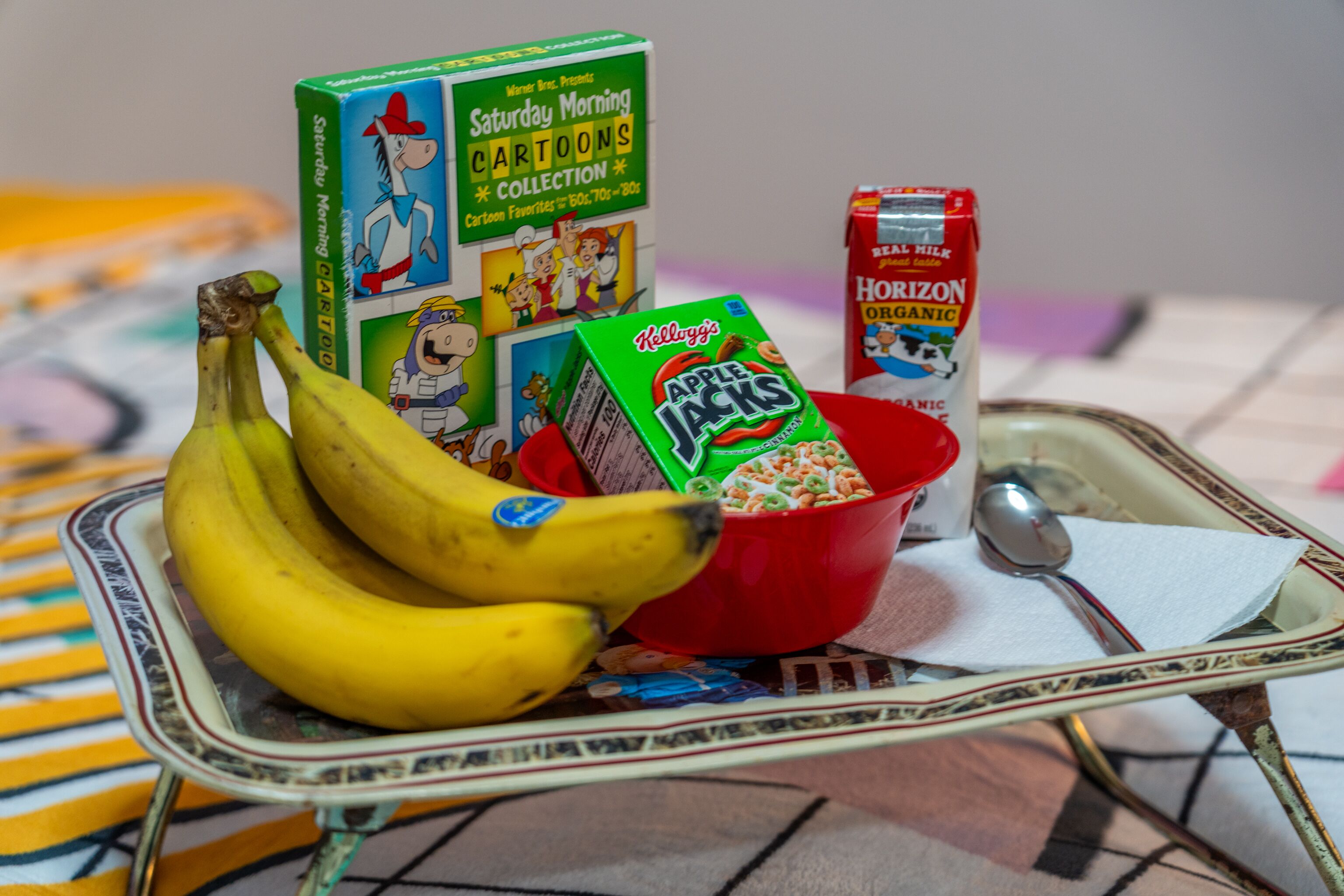 Een schaal met bananen, een kom met ontbijtgranen, een pak melk en een doos cornflakes.