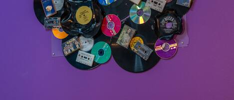 En säng med ett lila och gult överkast, en mjuk, lila kudde och en vägg dekorerad med olika cd-skivor och vinylskivor.