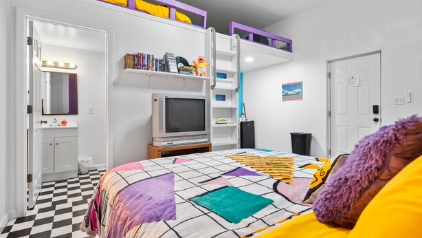 Een slaapkamer met een bed, een televisie, een boekenplank en een deur.