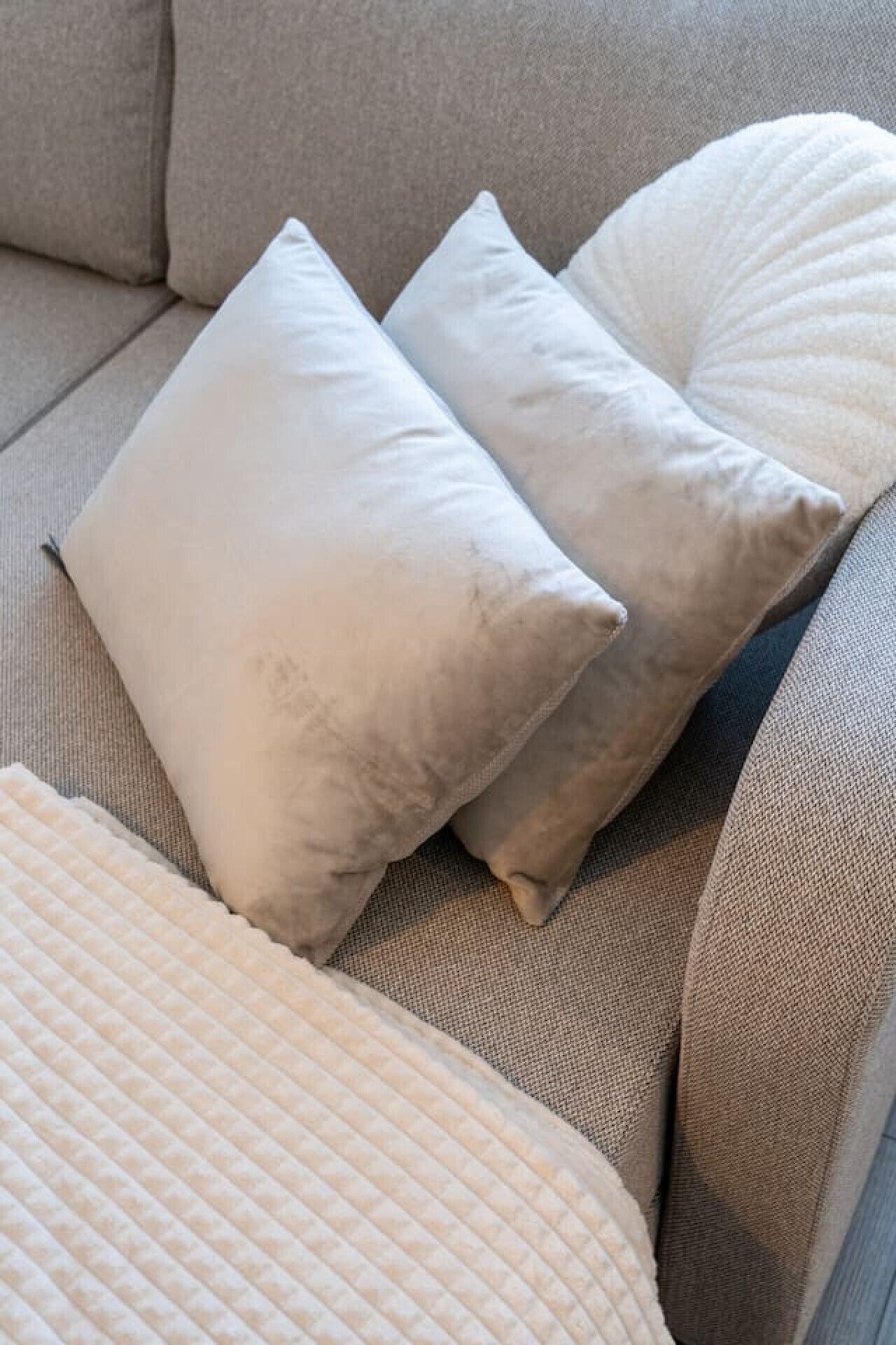Un sofá beige con dos almohadas blancas y un cojín blanco.