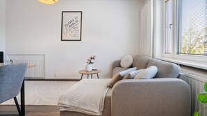 A modern living room with a grey sofa, a small round table with a vase of flowers, a framed picture on the wall, and a window with blinds. - Aurora City Studio By Lapland Host (Rovaniemi)