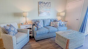 A living room with a blue sofa, two patterned armchairs, a coffee table, and a painting on the wall.
