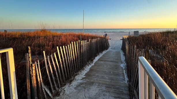 A wooden boardwalk leading to a beach with a clear sky.