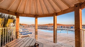A wooden deck with lounge chairs and a pool, under a wooden gazebo.