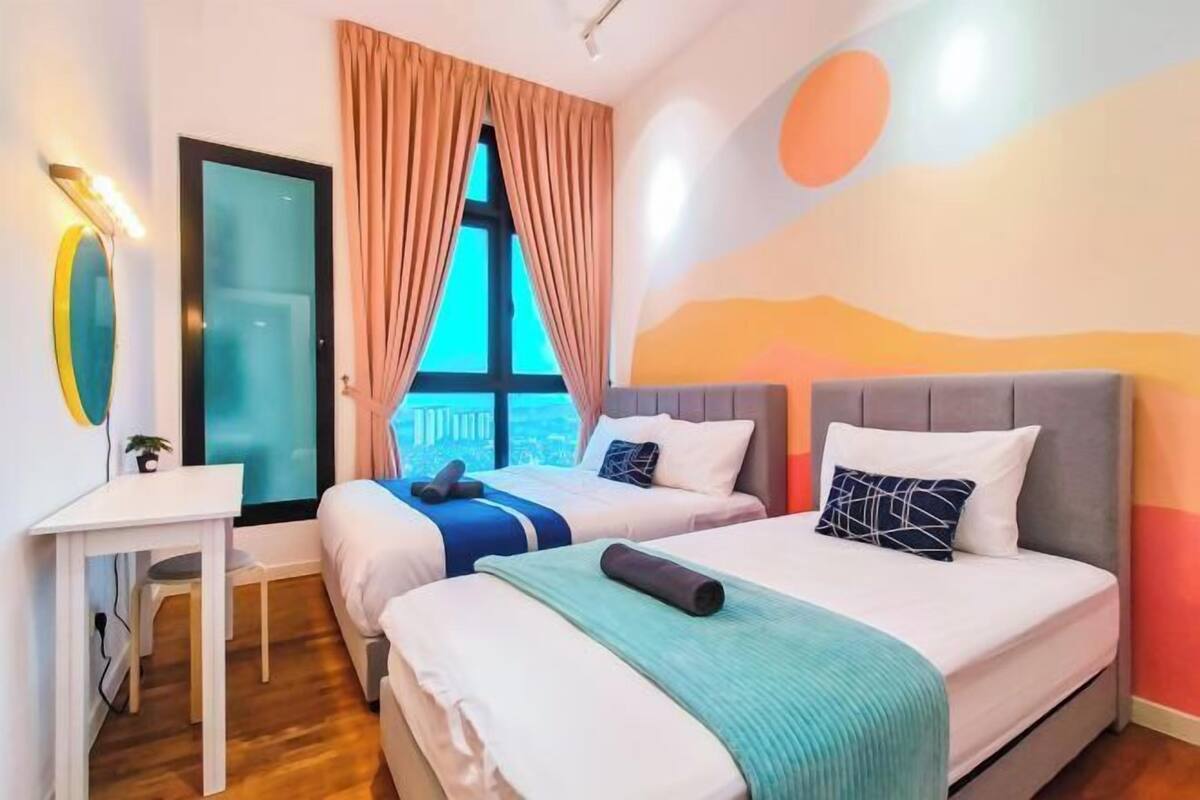 A hotel room with two beds, a desk, a chair, a window with curtains, and a wall with abstract art.
