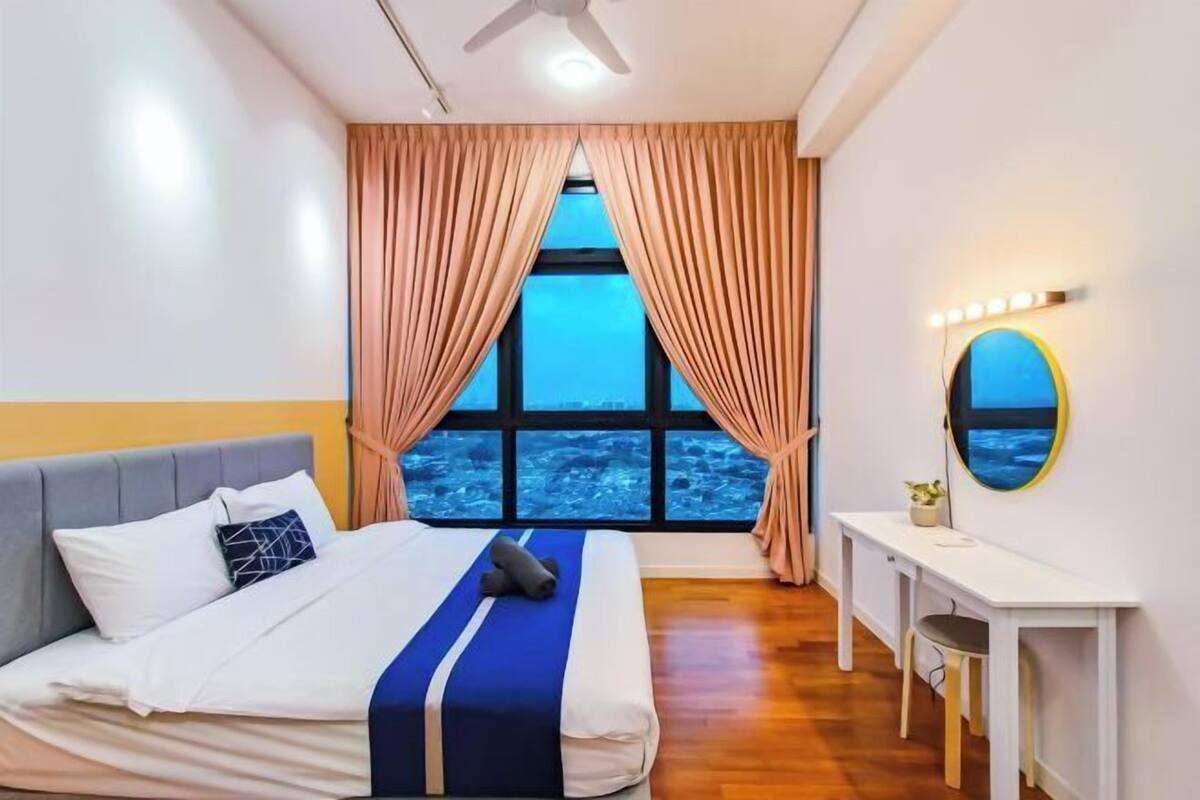A bedroom with a bed, a desk, a chair, a window with curtains, and a ceiling fan.