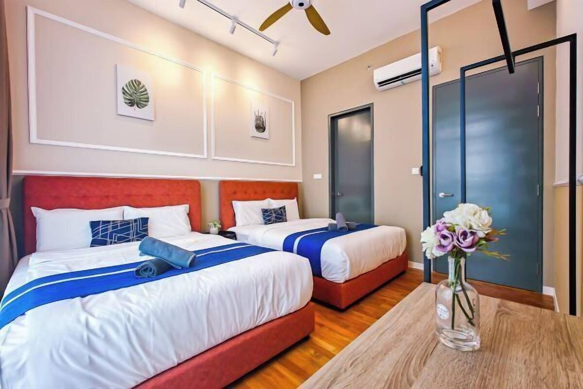 A hotel room with two beds, a wooden floor, a ceiling fan, and a vase with flowers on a table.