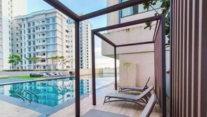 A modern outdoor lounge area with a pool, lounge chairs, and a view of high-rise buildings. - Skudai Paradigm Mall by RR JBcity (Tebrau)