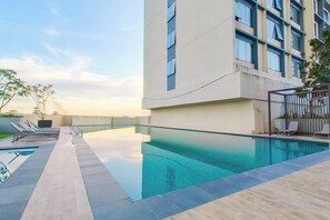Un hotel moderno con piscina infinita en la azotea, cielo despejado y vistas del horizonte urbano.