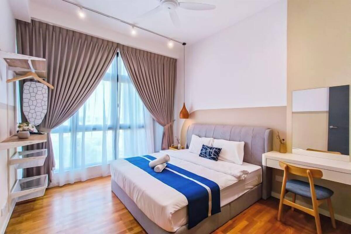A modern bedroom with a bed, desk, and chair, large windows with curtains, and a ceiling fan.