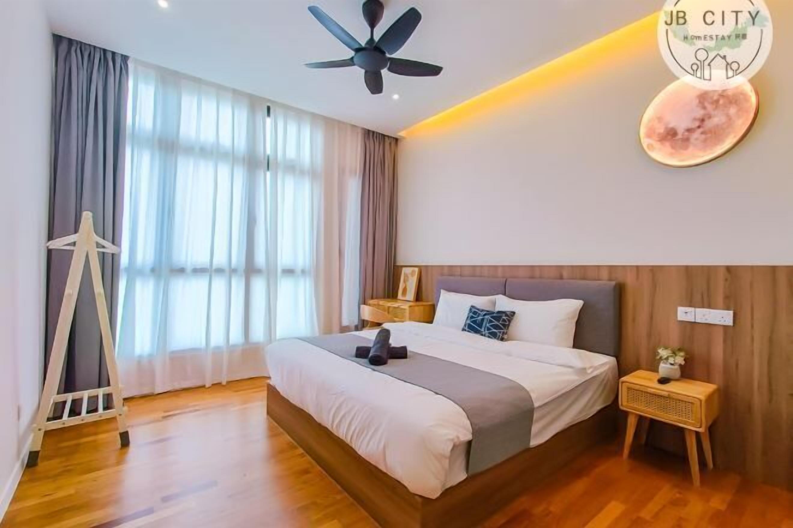 A modern bedroom with a large bed, a ceiling fan, a wooden floor, and a nightstand with a lamp.