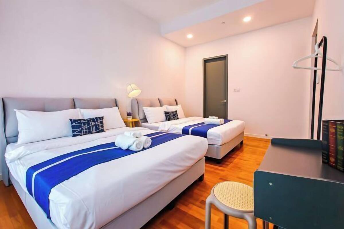 A hotel room with two beds, a desk, a chair, and a door.