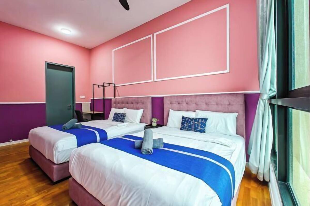 A hotel room with two beds, a purple accent wall, and a window with curtains.