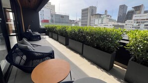 Eine Dachterrasse mit Sitzgelegenheiten im Freien, Topfpflanzen und Blick auf die Stadt.