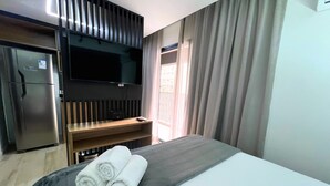 Ein Hotelzimmer mit Bett, Wandfernseher, Kühlschrank und einem Fenster mit Vorhängen.