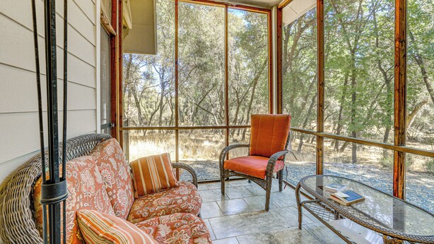 A sunlit room with a wicker sofa, a cushioned chair, and a glass table. - All-Season Outdoor Base Camp: Gold Country Home! (Fiddletown)