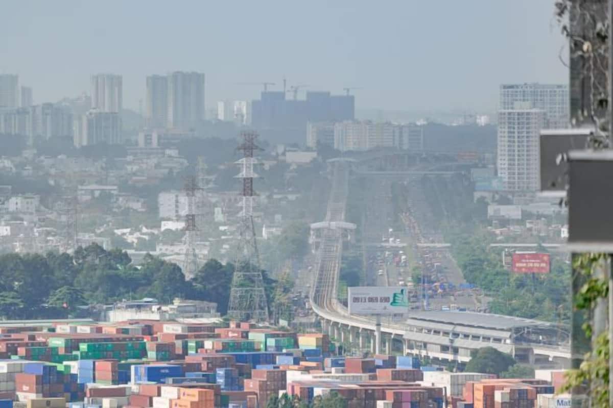 A cityscape with a large number of shipping containers, a highway, and high-rise buildings in the background.