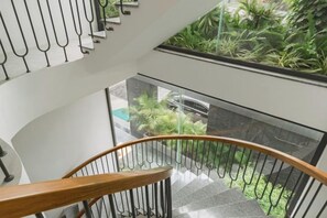 A modern staircase with a glass railing, leading to a lower level with a view of indoor plants. - Panda Garden Hotel &Apartment (Ho Chi Minh City)