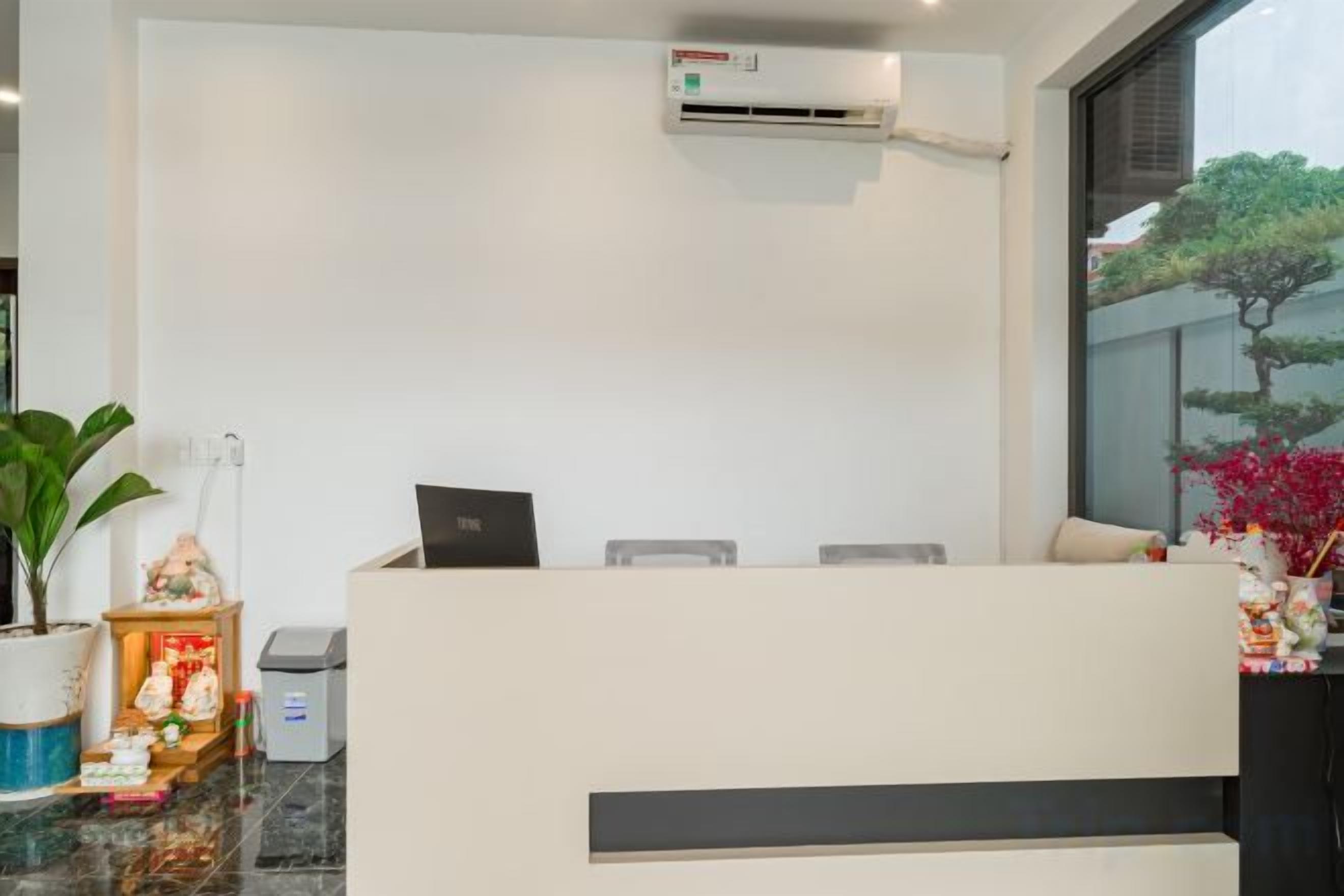 A reception desk with a laptop, a potted plant, and a small shrine.