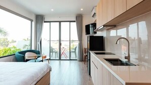 Una camera d'albergo moderna con un letto, angolo cottura, televisione e balcone con tavolo e sedie.