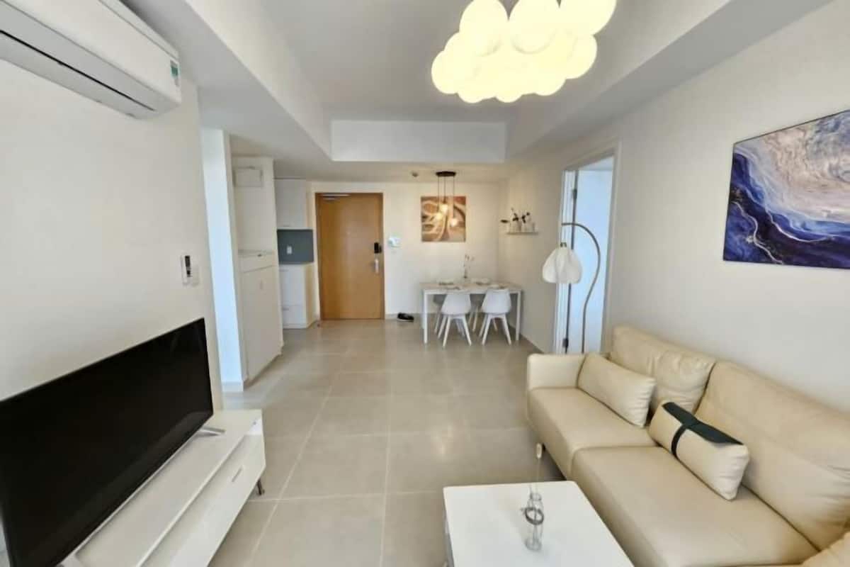 A modern living room with a flat-screen TV, a sofa, a coffee table, and a dining area in the background.