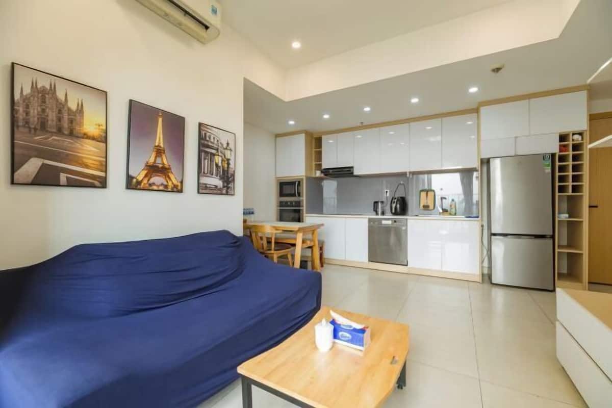 A modern living room with a sofa, a coffee table, and a kitchen area with cabinets and appliances.