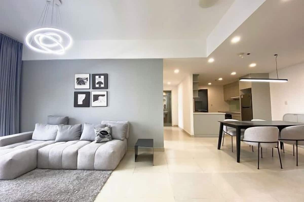 A modern living room with a sectional sofa, a dining table with chairs, and a kitchen in the background.