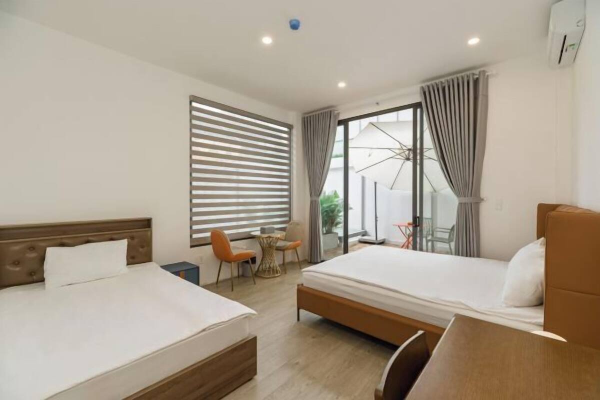 A modern hotel room with two beds, a small dining area, and a large sliding glass door to the outside.