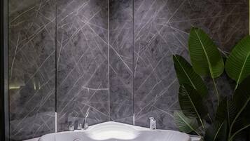 A bathroom with a freestanding bathtub, a marble wall, and a potted plant.