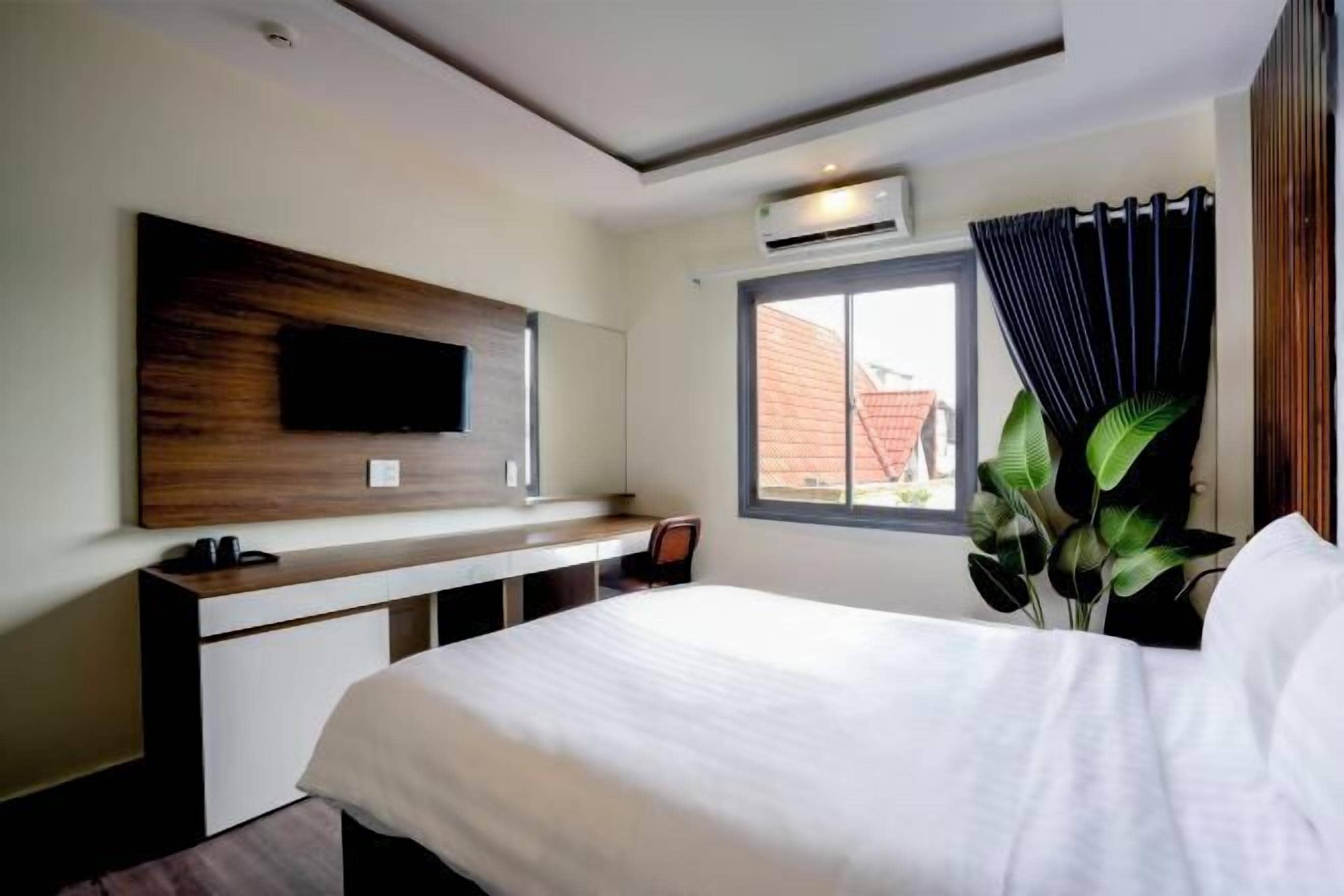 A modern hotel room with a bed, a desk, a flat-screen TV mounted on the wall, and a window with curtains.