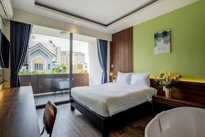 A hotel room with a bed, a desk, a chair, a window with curtains, and a view of buildings outside. - La Phan Huy Ich Hotel (Ho Chi Minh City)
