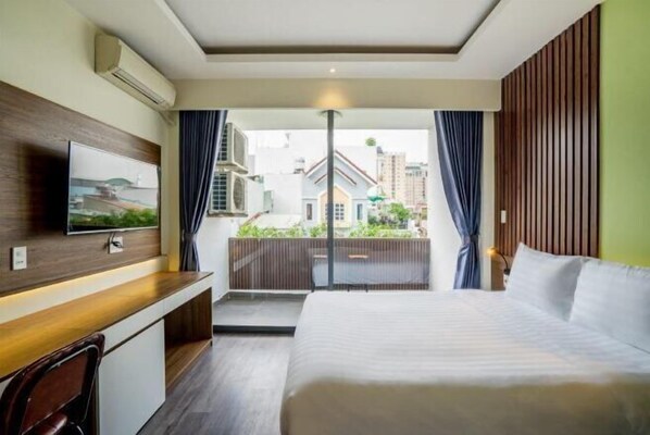 A hotel room with a bed, a desk with a chair, a TV mounted on the wall, and a view of the outside. - La Phan Huy Ich Hotel (Ho Chi Minh City)