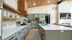 A modern kitchen with light green cabinets, a marble countertop, and a wooden ceiling. - Luxury 4BR Cabin on Pond for 18p- Pool, Sauna, Hot Tub & Game Room in Broken Bow (Broken Bow)