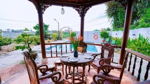 A covered outdoor seating area with a pool, surrounded by greenery and a cityscape in the background. - Tra Que Green Villa Hoi An (Hoi An)