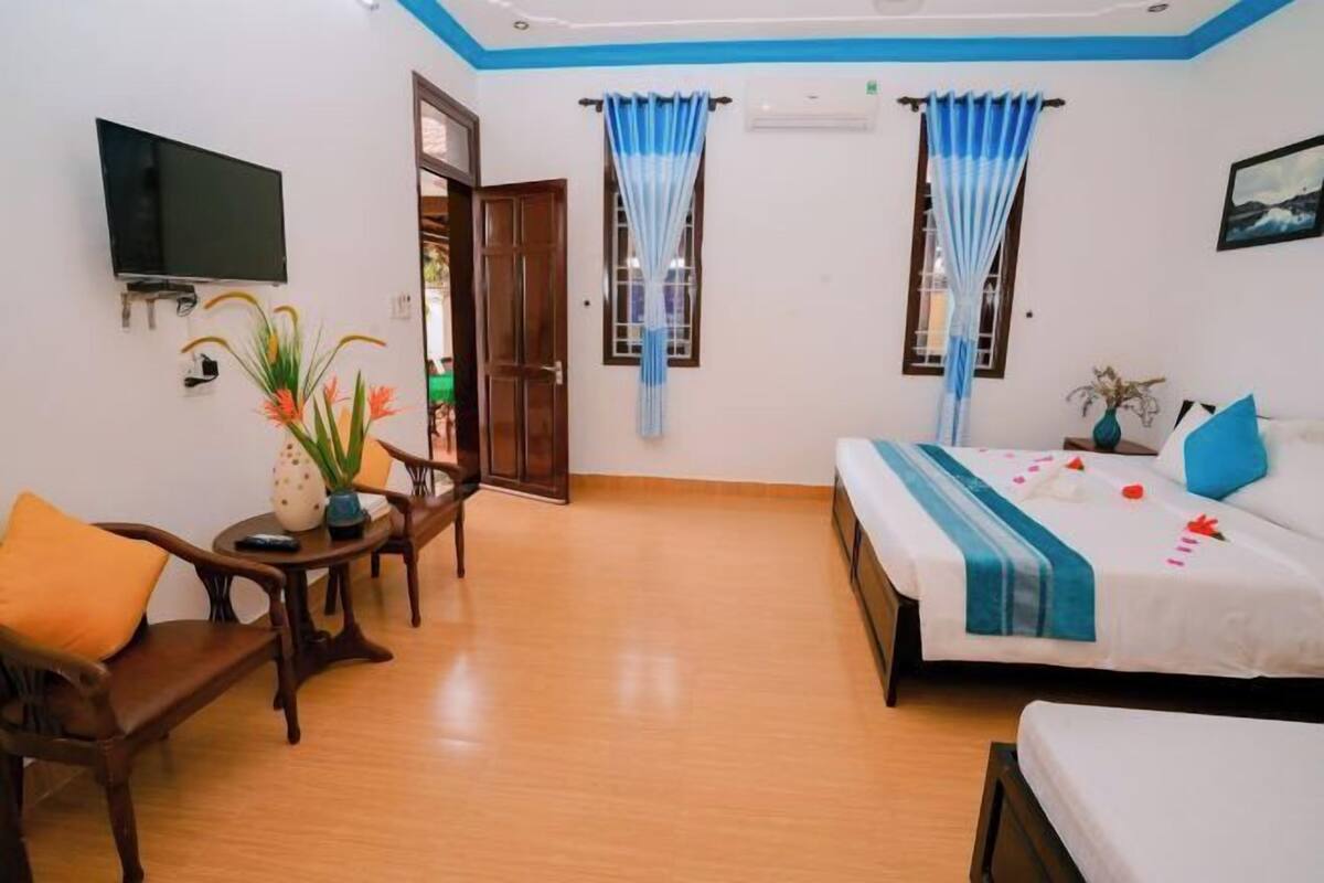 A room with a bed, a TV, a table with a vase, and a chair.