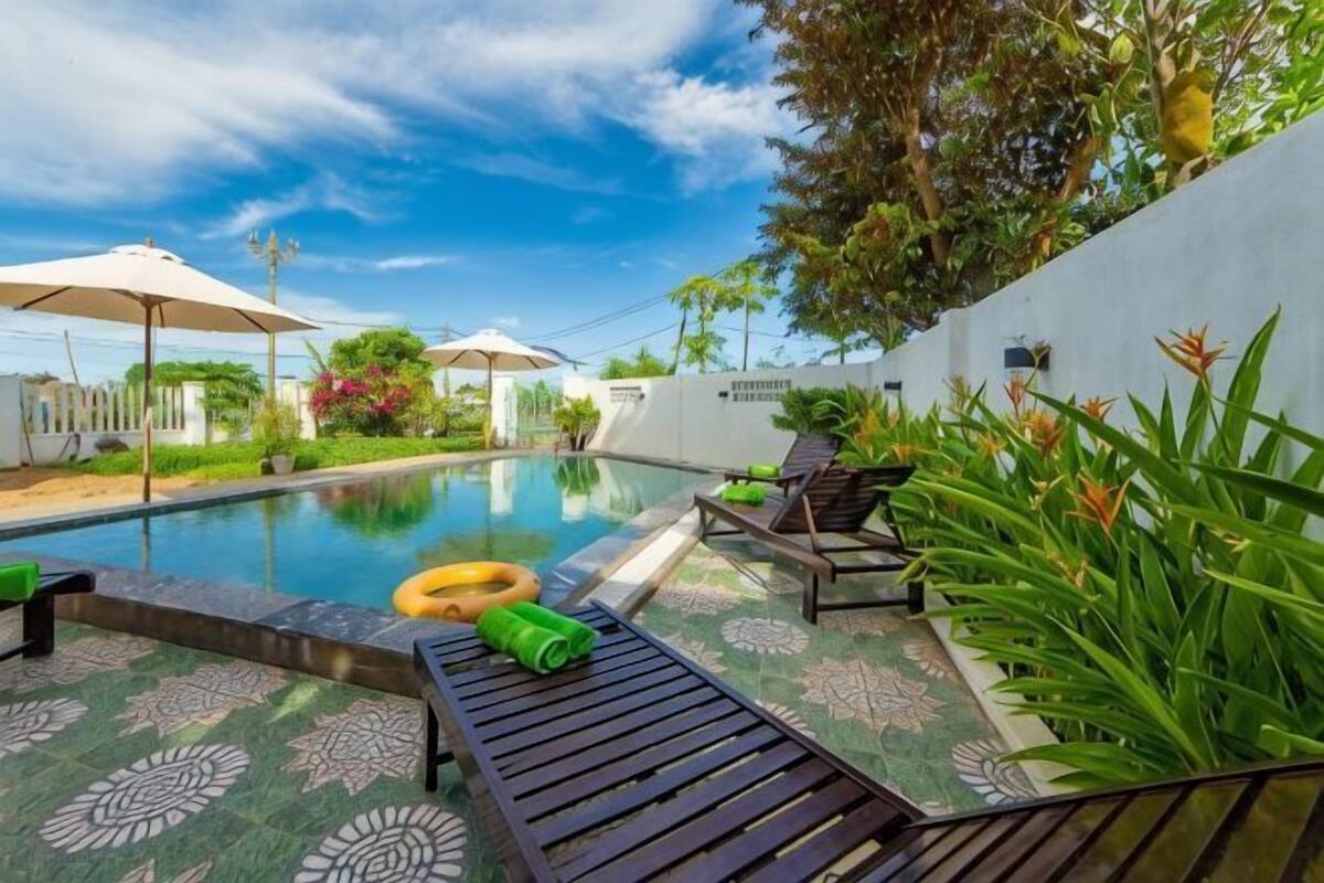 A pool area with lounge chairs, a floating ring, and umbrellas.